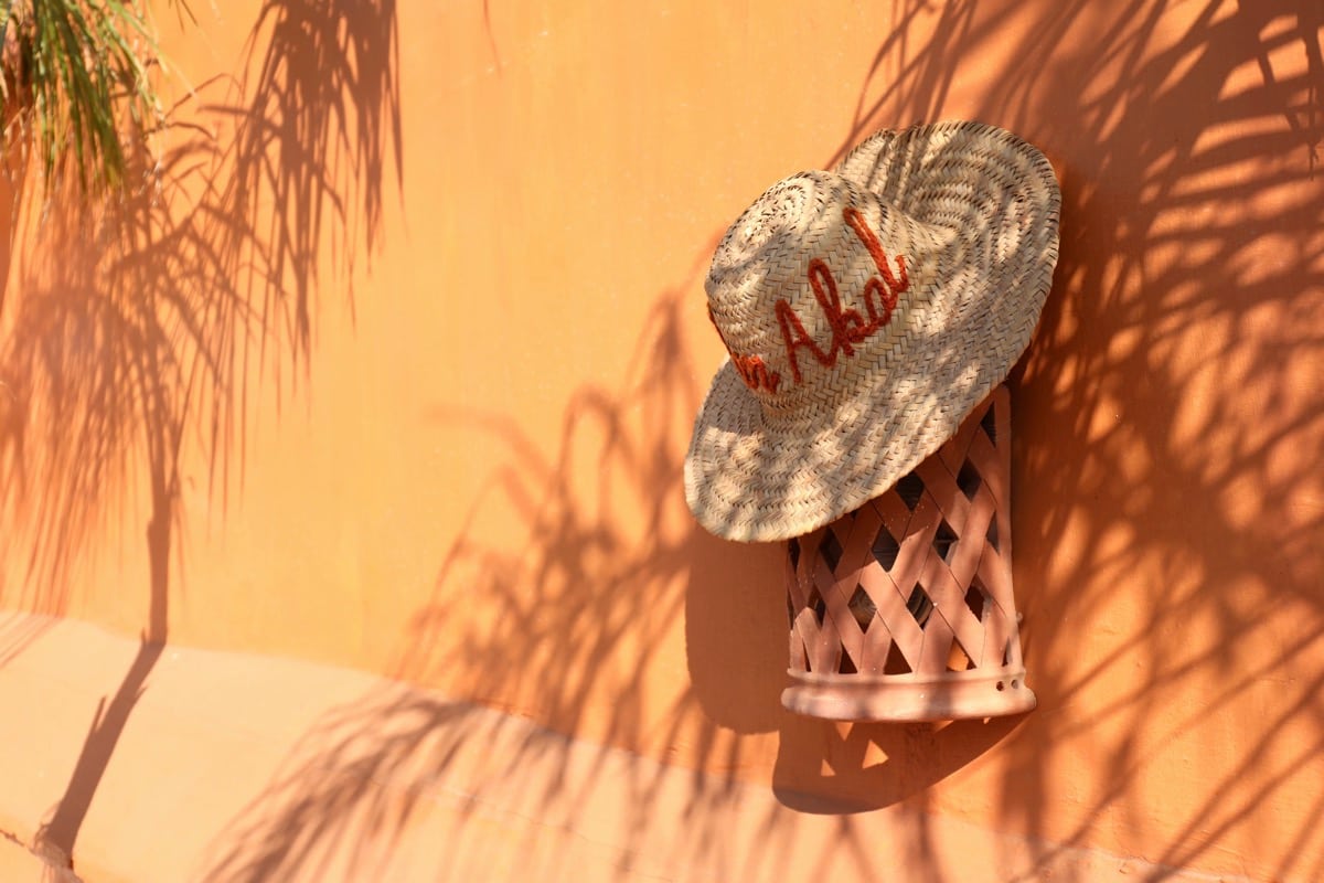 Un chapeau tressé Dar Akal entouré d’ombres de palmes sur un mur ocre